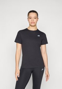 T-shirt noir à manches courtes en tissu doux, avec un petit logo bleu sur le côté supérieur gauche. À assortir avec des leggings noirs.