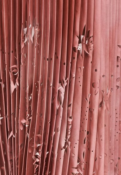 Papier rose plissé avec des motifs floraux découpés complexes et de petits trous partout, créant texture et intérêt visuel.