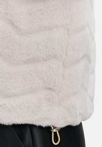 Rosa Kunstfelljacke mit einem strukturierten, gesteppten Muster und einem gelben Kordelzugakzent am Saum; darunter sichtbares schwarzes Leder.