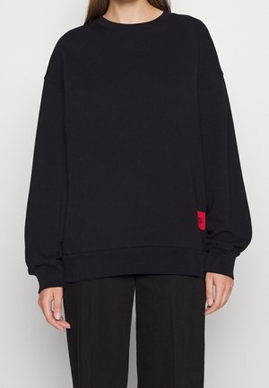 Zwarte sweatshirt van katoen, met een ronde hals, doorgezakte schouders en elastische manchetten. Heeft een klein rood label aan de zijkant.