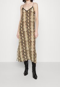 Gul- og sort slangeprint slipkjole med tynde spaghetti-stropper, der har en V-udskæring og en flydende silhuet, der når til midten af læggen.