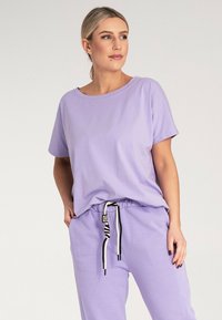 Jasnofioletowa bawełniana koszulka z krótkim rękawem i szerokim dekoltem, w komplecie z pasującymi spodniami z troczkiem i czarnymi akcentami.