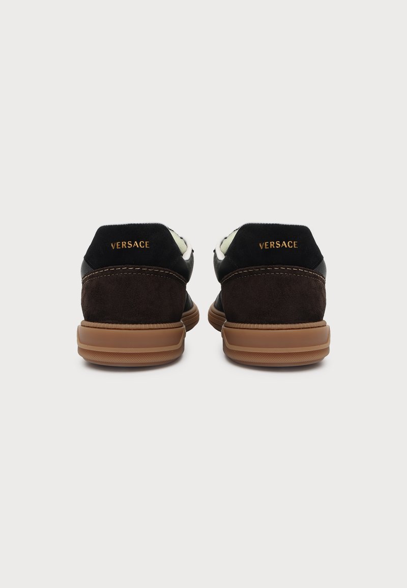 Ein Paar braune und schwarze Versace-Sneaker von hinten gezeigt, mit goldener Versace-Beschriftung an der Ferse und hellbraunen Gummisohlen.
