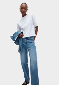 Weißes kurzärmeliges T-Shirt, blaue hoch geschnittene Jeans und Jeansjacke. Lässiger Schnitt, Jeans in mittlerer Waschung, minimale Abnutzung, glatte Textur.