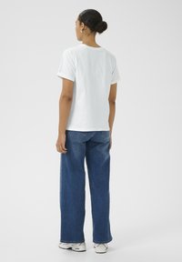 Camiseta blanca de algodón con mangas enrolladas y pantalones de mezclilla de pierna ancha. El modelo lleva zapatillas blancas, mostrando un diseño minimalista y casual.