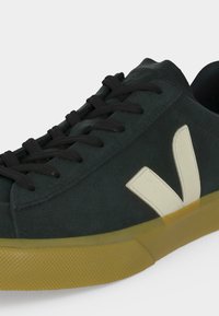 Baskets en daim vert foncé avec des lacets noirs, un logo V blanc sur le côté et une semelle en caoutchouc jaune translucide.