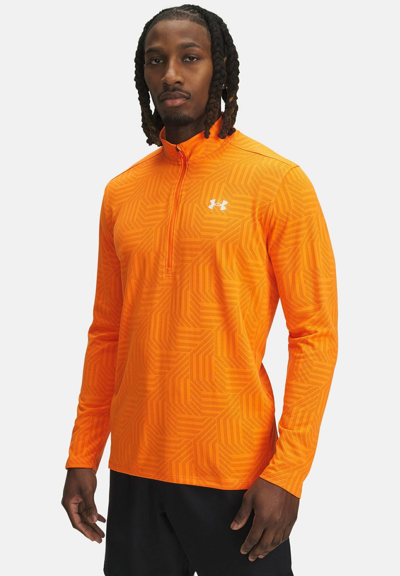 Oranžinė ketvirčio užtrauktuku ilgomis rankovėmis palaidinė su geometriniu raštu, pagaminta iš lengvos medžiagos. Yra mažas baltas logotipas ant krūtinės.