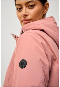 Roze waterdichte jas met capuchon, voorzien van een zwart rond logo-patch op de mouw. Glad textuur en een getailleerd ontwerp.