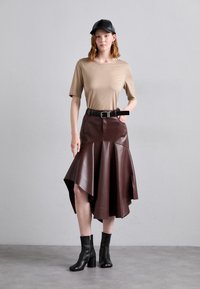 Un top scurt bej cu mânecă scurtă, asociat cu o fustă burgundă din piele ecologică, cu talie înaltă și lungime până la genunchi, având un tiv evazat și o curea neagră. Botine negre până la gleznă.