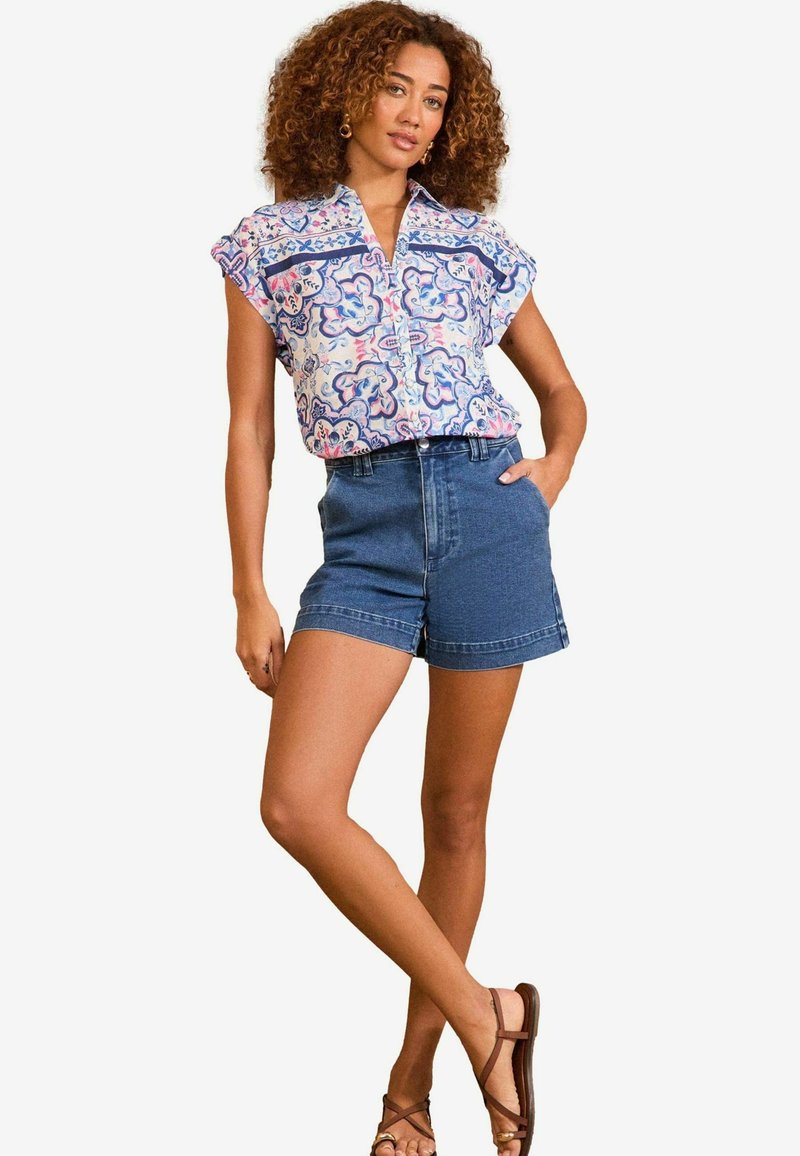 Trykt kortærmet skjorte med blå og pink blomsterdesign, parret med højrejsede denimshorts. Sandaler med krydsskårne stropper fuldender outfittet.