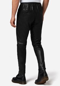 Zwarte leren broeken met een elastische tailleband, achterzakken en ritsen langs de benen. Glad textuur en tappere pasvorm.