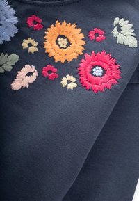 Tessuto blu scuro con ricami floreali colorati in rosso, arancione, rosa, lavanda e accenti verdi in diverse forme e dimensioni.