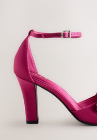 Roze satijnen sandaal met hoge hak, afgeronde neus en enkelbandje, met een slanke vorm en een glanzende afwerking. Versterkte hiel voor extra stabiliteit.