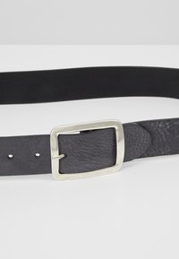 Schwarzer Lederarmband mit strukturierter Oberfläche, einer silbernen rechteckigen Schnalle und mehreren Verstelllöchern entlang des Riemens.