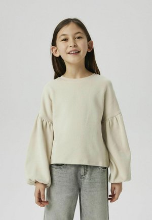 Lichtbeige langarm gebreid top met ballonmouwen, ronde halslijn en een ontspannen pasvorm, gecombineerd met lichtgrijze rechte jeans.