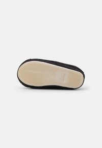 Black shoe sole made of rubber with a textured surface. Features a cream-colored outline and subtle wavy pattern for traction.