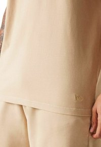 T-shirt in cotone beige a maniche corte, con un logo sottile in filo coordinato vicino all'orlo. Texture morbida e vestibilità rilassata.