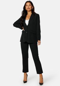 Czarna skrojona marynarka z zapięciem na jeden guzik, klapami typu notch oraz dwiema przednimi kieszeniami, zestawiona z dopasowanymi czarnymi spodniami i szpilkami.