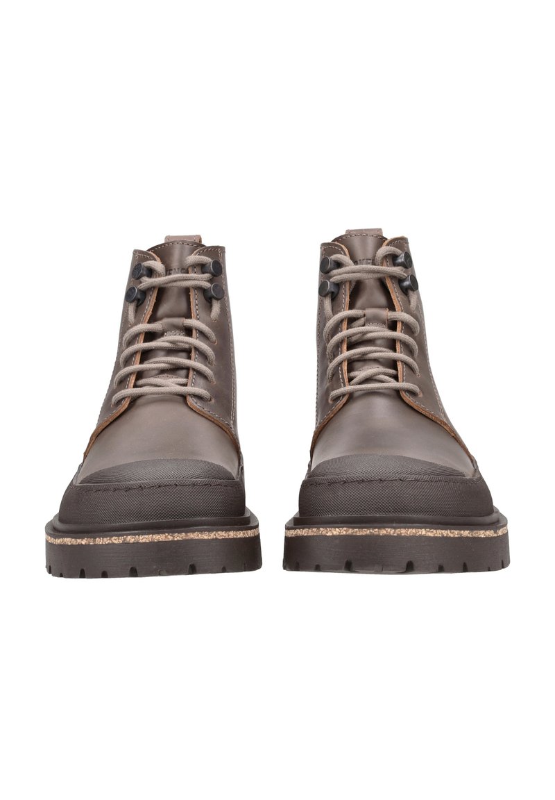 Stivali alla caviglia in pelle marrone con punta arrotondata, colletto imbottito e cuciture a contrasto. Presentano occhielli in metallo e una suola in gomma testurizzata.