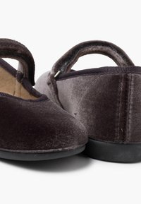 Mocasines de terciopelo oscuro con punta redondeada y correa elástica. Presentan una textura suave, suela de goma negra y detalles de costura mínimos.