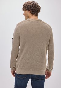 Beige gebreide trui met textuursteek, ribbels bij de manchetten en onderkant, in een effen kleur zonder zichtbare patronen of logo's.