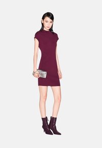 Abito bodycon bordeaux con maniche corte, texture a coste e colletto alto. Abbinato a stivali alla caviglia con punta affusolata e una clutch metallica.