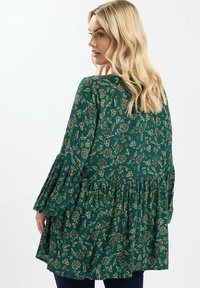 Top verde con motivo floreale, dal taglio morbido, maniche a campana e orlo con volants a strati. Realizzato in un tessuto texturizzato.