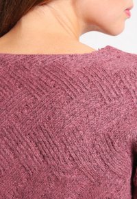 Maglione a maglia texturizzata in un profondo color mauve, con un motivo a spina di pesce. Materiale morbido e peloso con scollo ampio e bordi a coste.