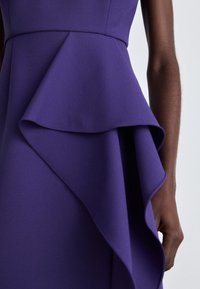 Lila Kleid mit einem weichen, strukturierten Stoff, einer geschichteten Rüschendetail an der Taille und einem taillierten Oberteil.