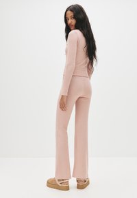 Top in maglina rosa pastello aderente e pantaloni svasati in tessuto morbido, con dettagli a coste sull'orlo. Scarpe con plateau chunky e accentuazione in pelliccia e shearling.