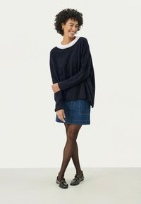 Maglione navy con scollatura ampia, colletto bianco; abbinato a una gonna di jeans e scarpe nere. Materiali testurizzati, vestibilità rilassata.