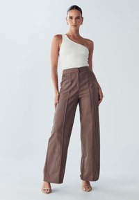Brązowe szerokie spodnie z wysokim stanem, przodu z plisami i gładką teksturą, połączone z dopasowanym białym topem na jedno ramię z żebrowanego materiału.