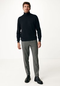 Svart polotröja, figurnära stil. Grå rutiga byxor, skräddarsydd passform, uppvikta vid vristen. Svarta läderankelboots med grova sulor.