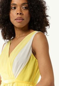 Gelbes und weißes Kleid mit V-Ausschnitt, elastischem Bund und fließendem Stoff, der ein diagonales Farbblockmuster zeigt. Leichte Textur.