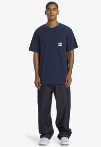 Námorně modré bavlněné tričko s kapsou na hrudi a bílým logem. Vytvořeno s volně střiženými tmavými džínami a bílými teniskami.