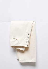 Pantalones de algodón beige enrollados con un bolsillo frontal, que cuentan con botones de metal a lo largo del costado y un dobladillo cosido. Textura suave.