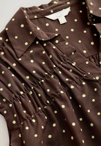 Barna len blúz sárga pöttyökkel, ráncolt derékkal, rövid gallérral és látható "Next" márkajelzéssel.