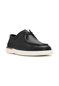 Chaussure en cuir noire avec un bout rond, semelle en caoutchouc blanche et détails cousus. Présente des lacets fins et un design bas.