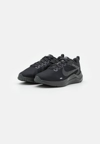 Zapatillas deportivas negras con una parte superior de malla texturizada, puntera reforzada y suela de goma. Las características incluyen cordones, acentos de logo y una suela acolchada.