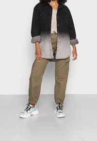 Camicia di jeans black to grey ombre, top in maglia beige, pantaloni cargo oliva e sneakers bianche con dettagli neri e blu, dotate di chiusura con lacci e suola in gomma.