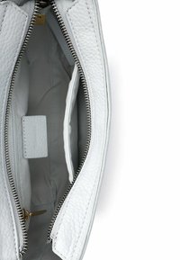Wnętrze białej skórzanej torebki, z teksturowaną powierzchnią, srebrnym zamkiem błyskawicznym i jedną kieszenią. Gładka jasnoszara podszewka poprawia widoczność.