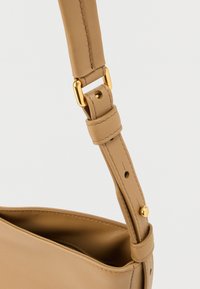 Τσάντα χειρός σε ταμπά δέρμα με ομαλή υφή, διακοσμημένη με αγκράφα σε χρυσό τόνο και ρυθμιζόμενο ιμάντα, τονίζοντας καθαρές γραμμές και μινιμαλιστικό σχεδιασμό.