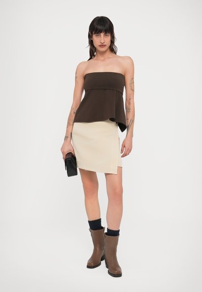 Καφέ τοπ χωρίς τιράντες με σχέδιο πεπλούμ, σε συνδυασμό με μπεζ μίνι φούστα με διαγώνιο τελείωμα. Συνδυασμένο με καφέ μπότες μέχρι το γόνατο και μαύρη τσάντα.