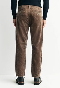 Brown corduroy pants with vertical ribbed texture, featuring two back pockets and a relaxed fit, paired with black ankle boots.