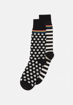 Schwarze Socken mit weißen gepunkteten Motiven auf einer Seite und schwarz-weißen Streifen auf der anderen Seite, mit einem farbenfrohen gestreiften Bündchen.