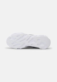 Sneaker talpa textúrált fehér gumiból készült, hullámforma mintával és barázdákkal a tapadásért. Fekete felsőrész látható a szélein.