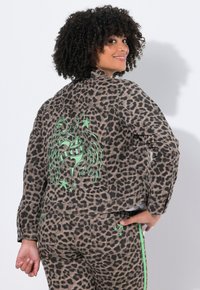 Denimjacka med leopardtryck som har en grön broderad design och stjärnaccenter på ryggen, med en figurnära kropp och långa ärmar.