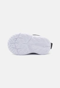 Chaussure de sport noire avec une semelle en caoutchouc blanc texturé présentant un motif en zigzag et le logo "Nike", conçue pour l'adhérence et la durabilité.
