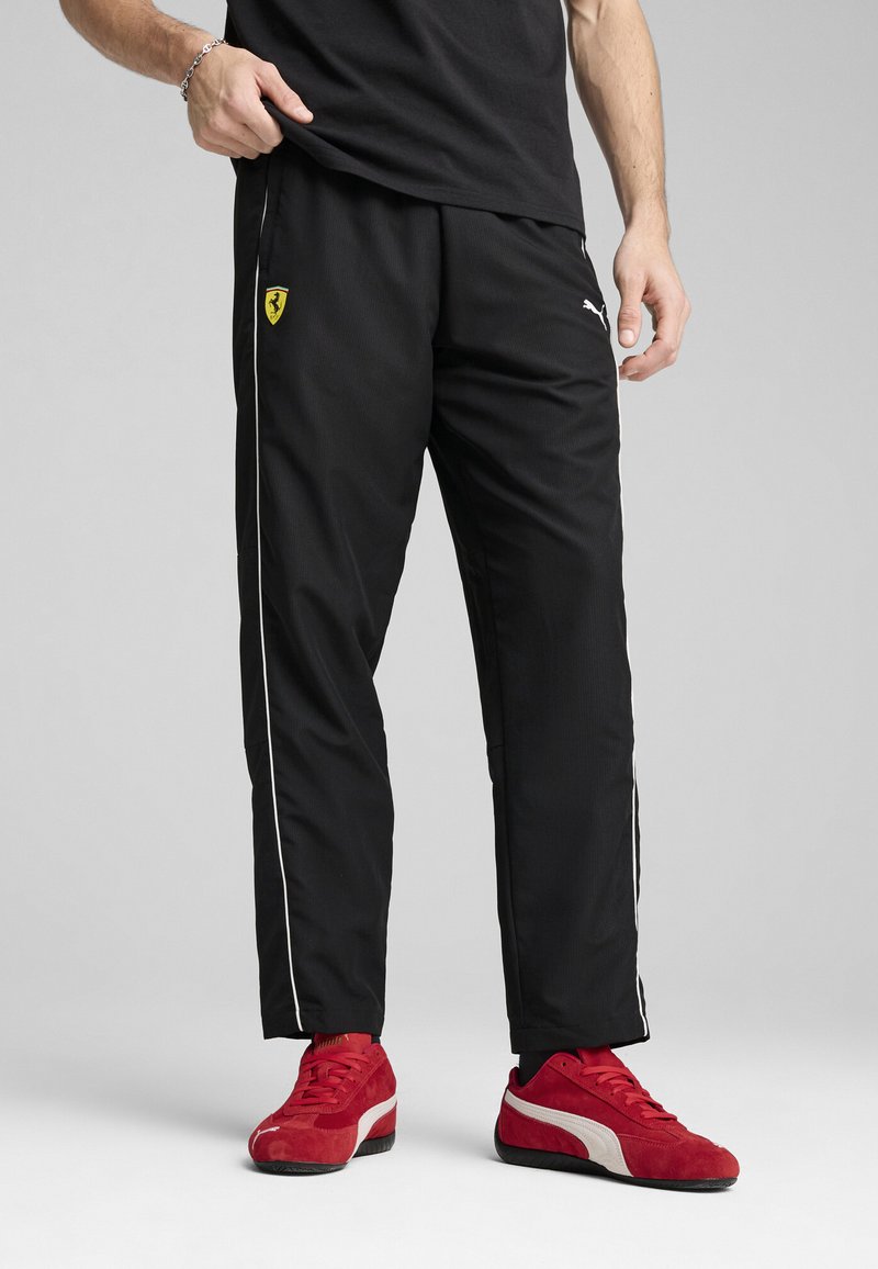 Sorte track pants med hvide sideløb, prydet med et gult Ferrari-logo. Kombineret med røde ruskinds sneakers. Casual design, letvægtsstof.