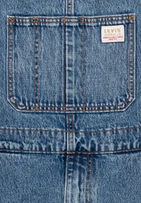 Blå denimöveralls med en rektangulär bakficka, orange sömmar och en Levi's etikett med röd och vit färg.